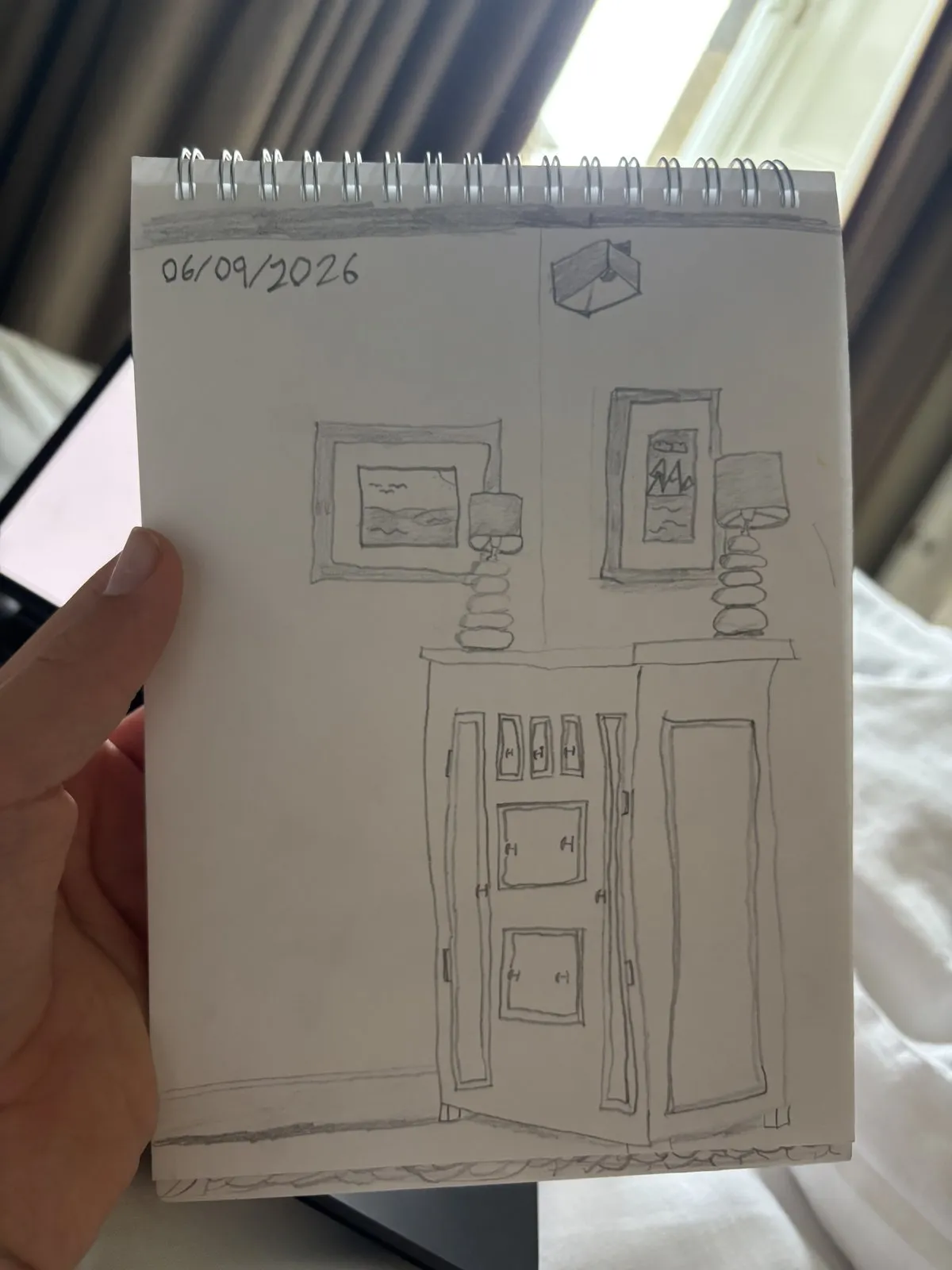 A pencil sketchbook drawing of a tall cabinet, lamps, and wall art in perspective.