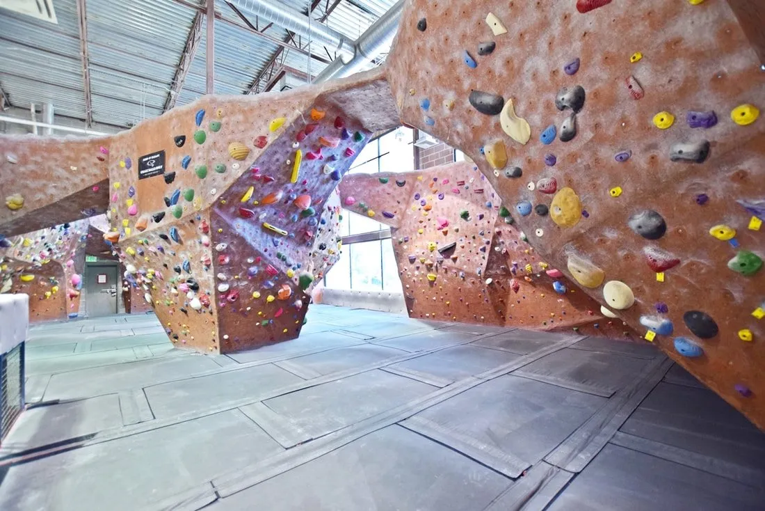 An indoor rock climbing gym with padded flooring and colorful holds on bouldering walls.