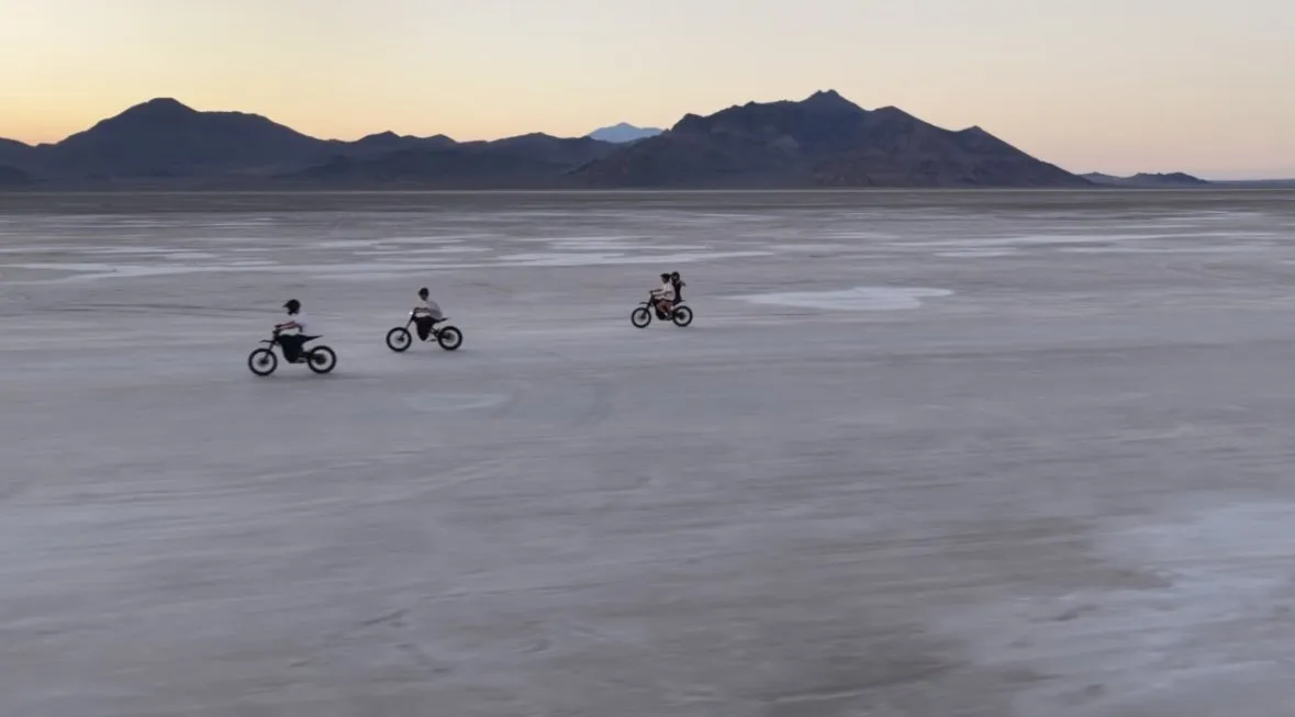 Three riders on recreational bikes across a flat desert expanse at sunset.