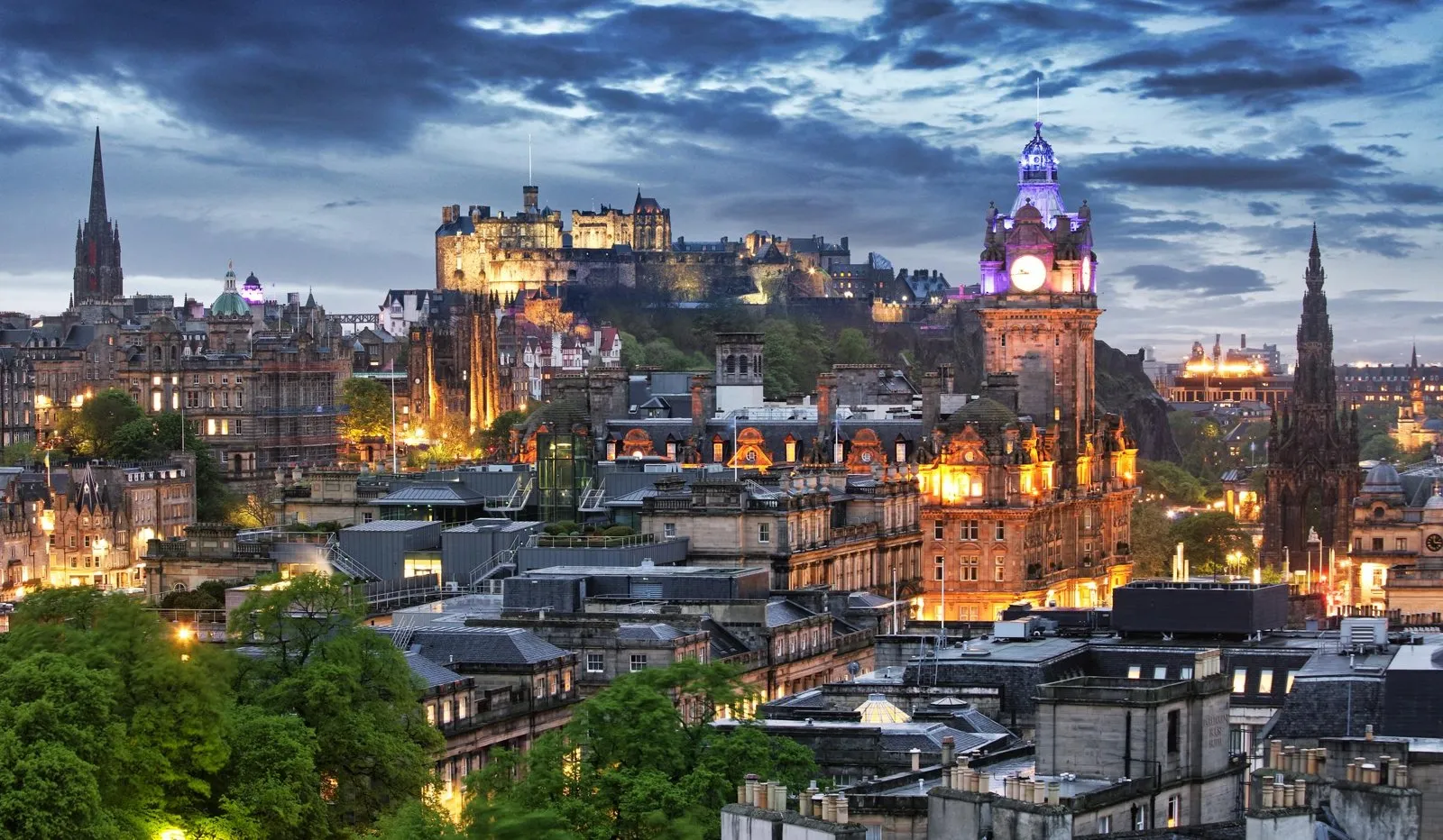 Elevated panoramic view over the historic stone buildings and clock tower of Edinburgh at dusk.