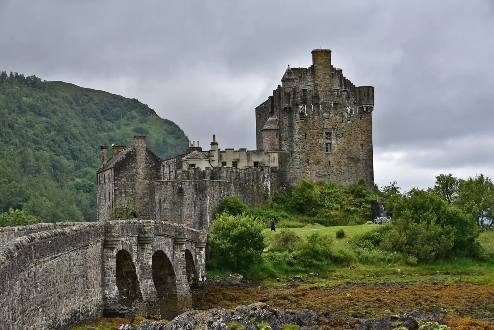 Eilean Donan Castle with its stone footbridge over tidal waters beneath an overcast sky.