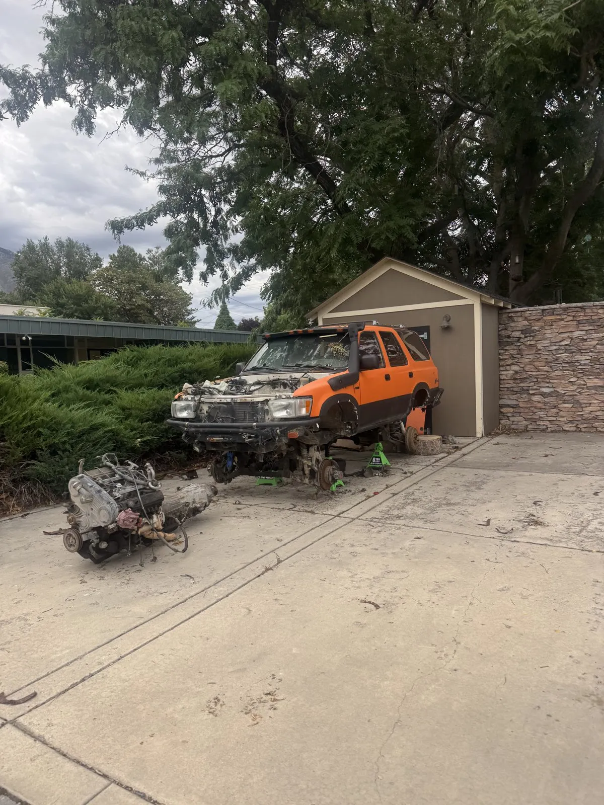 A disassembled truck engine and chassis sitting in a residential driveway.