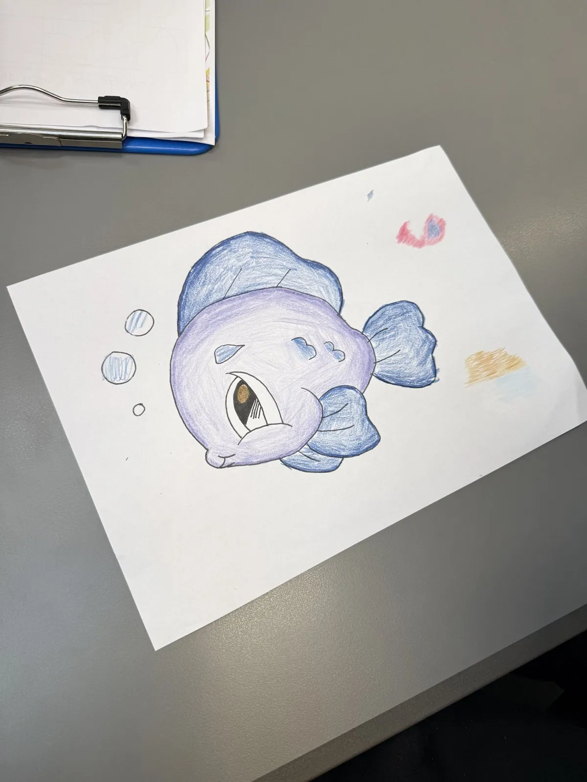 A colored pencil drawing of a stylized purple and blue fish on white paper.