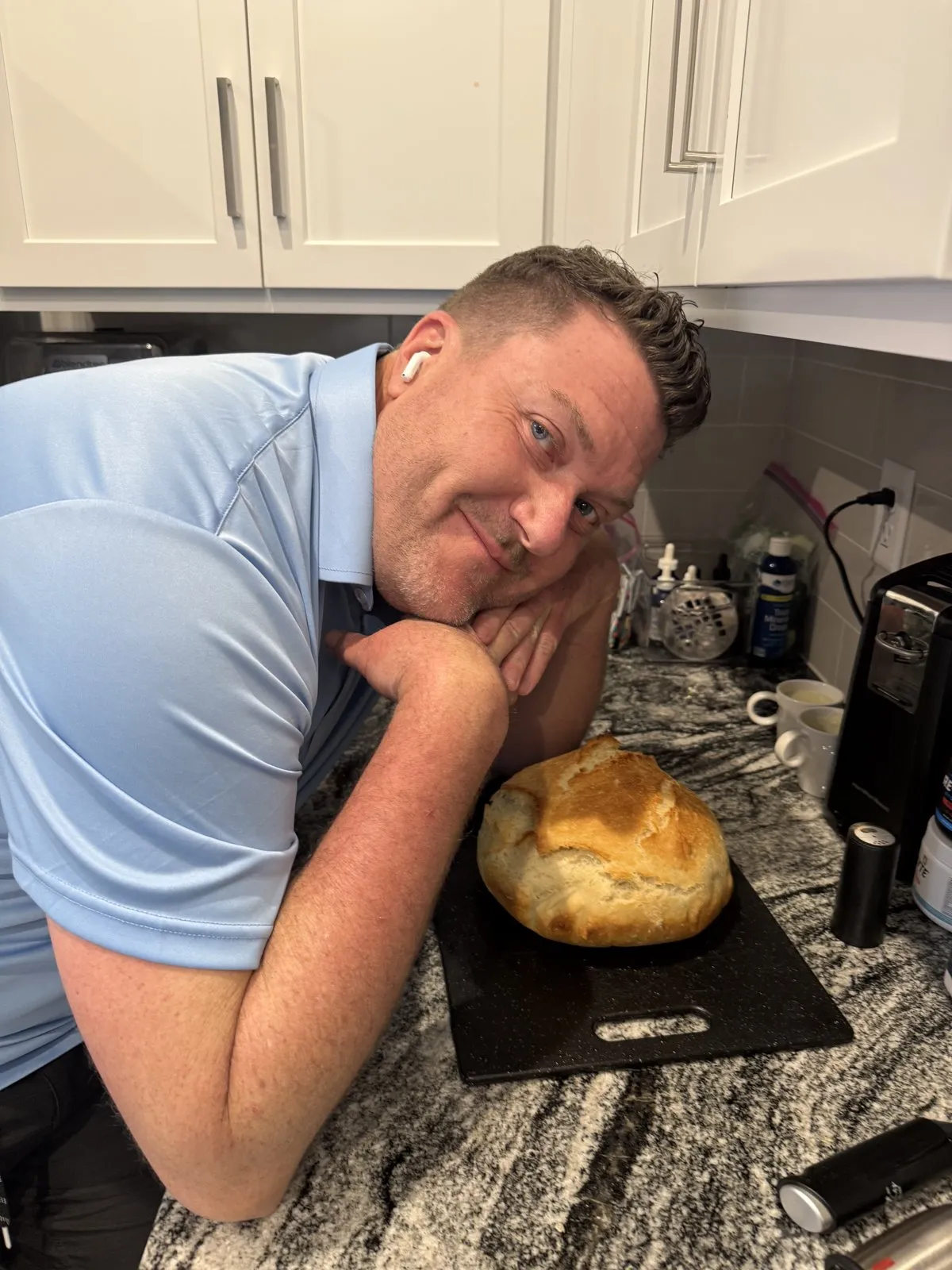 A freshly baked golden round loaf of bread resting on a black cutting board.