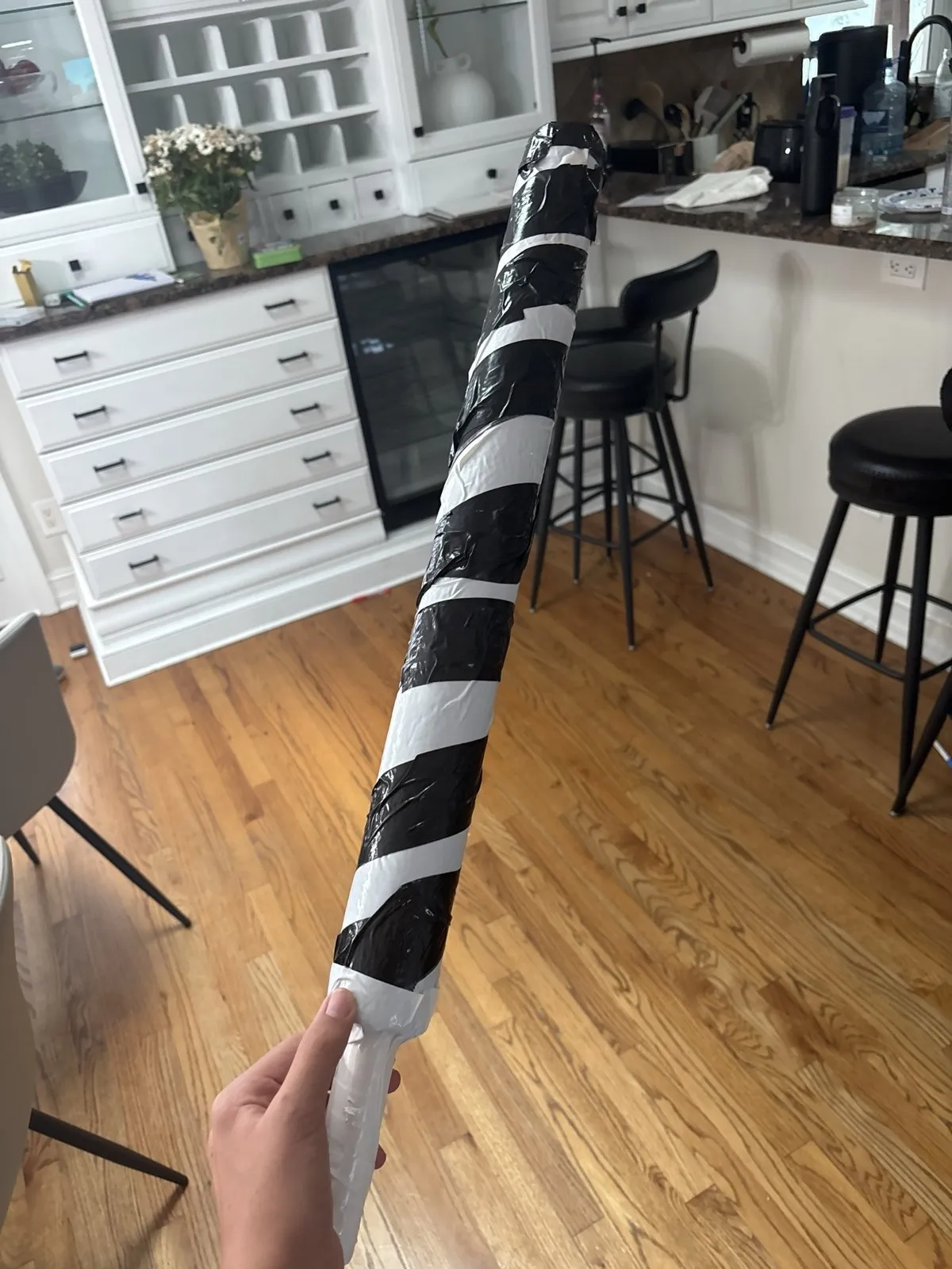 A hand holding a fabricated cylindrical prop wrapped in black and white tape.