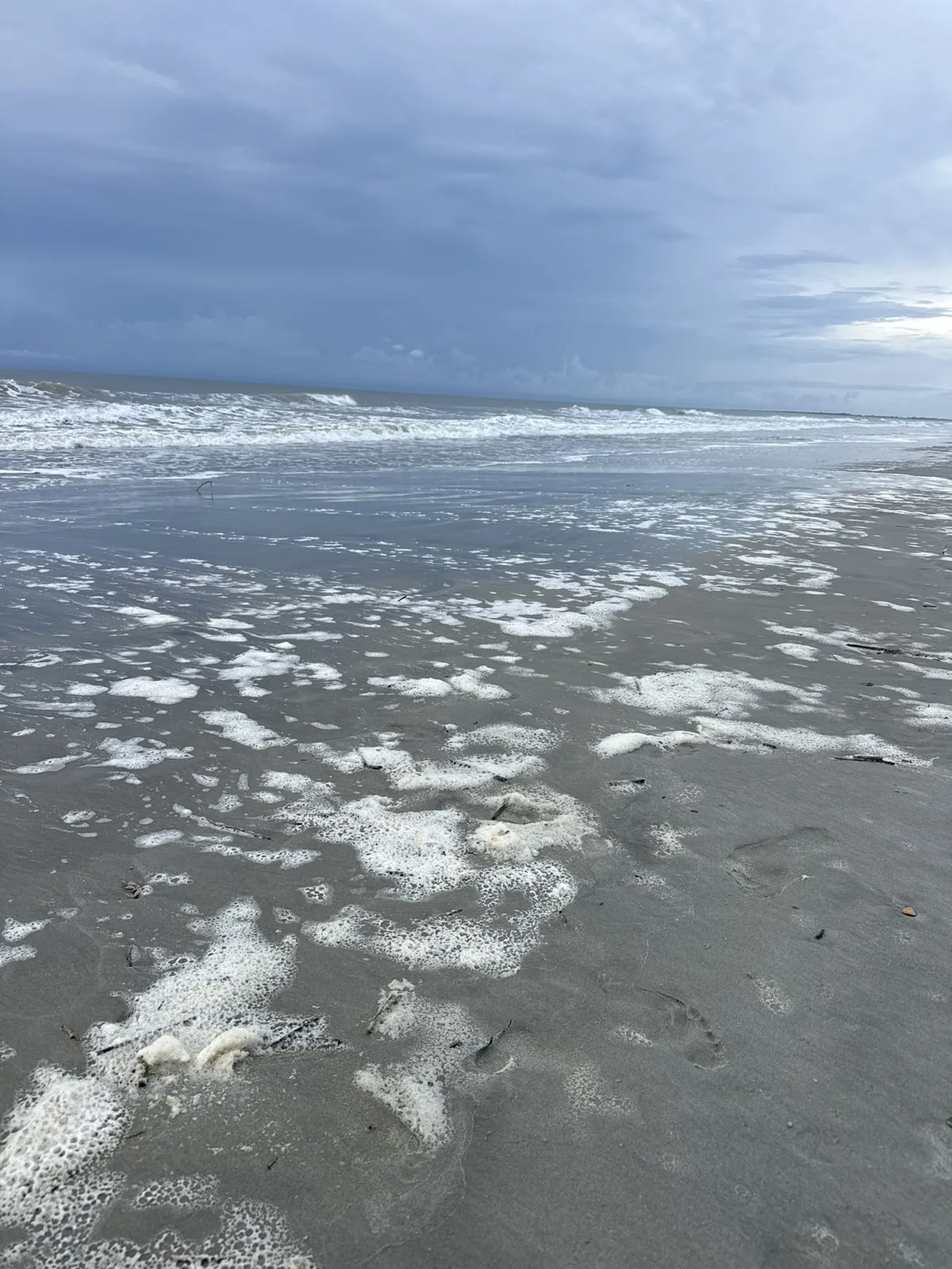 Sea foam spreading across the sand along an ocean coastline.