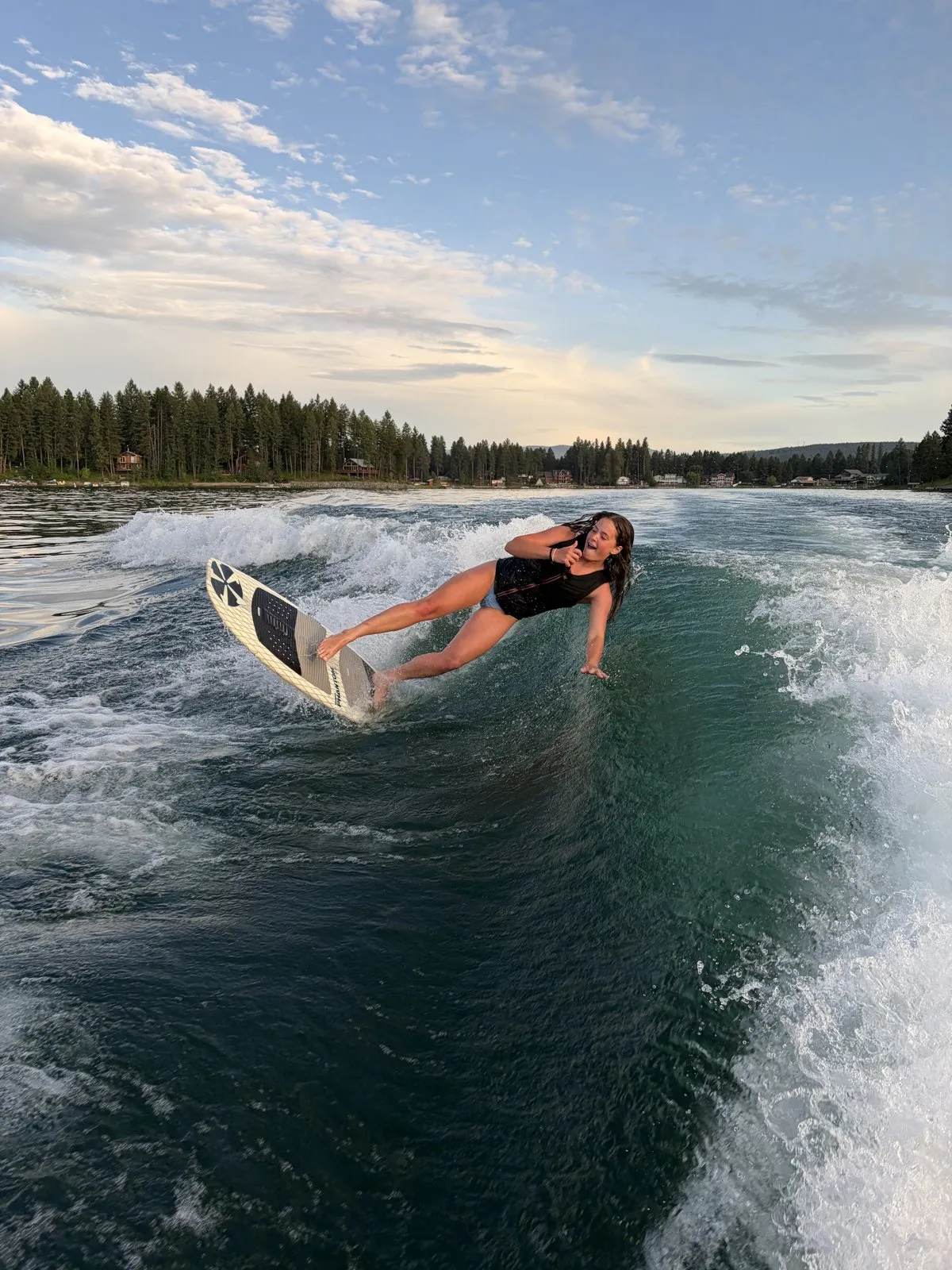 A person riding a wake surf board along the boat wake at sunset.