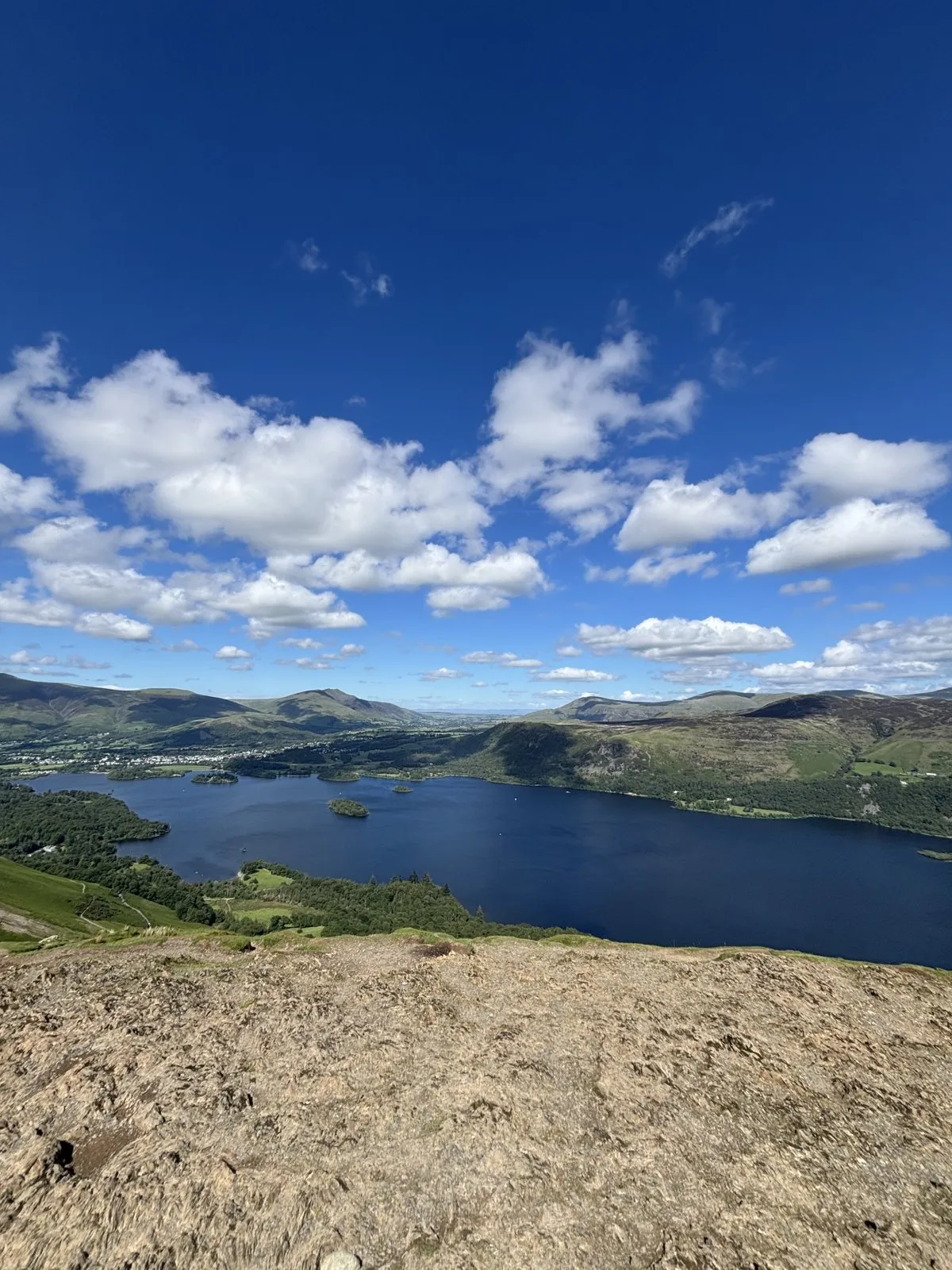Panoramic view of a deep blue lake nestled among rolling mountains under a bright blue sky.